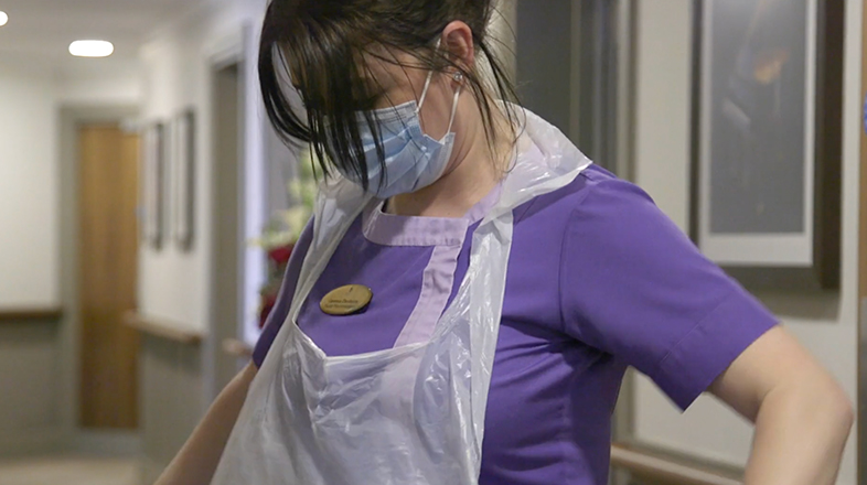 A nurse putting on an apron