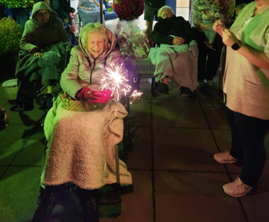 Residents and guests at Beechgrove Care Home enjoying a colourful fireworks display in the garden, surrounded by family, friends, and cosy cups of hot chocolate.