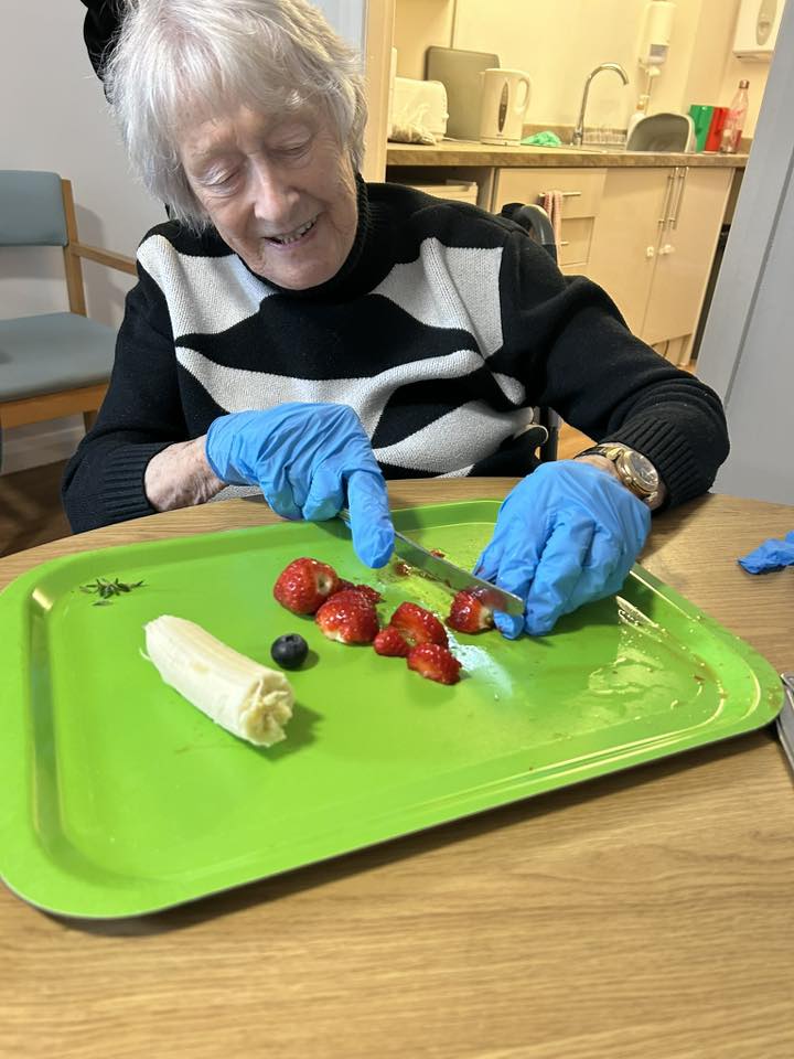 older lady sat down with blue gloves cutting fruit