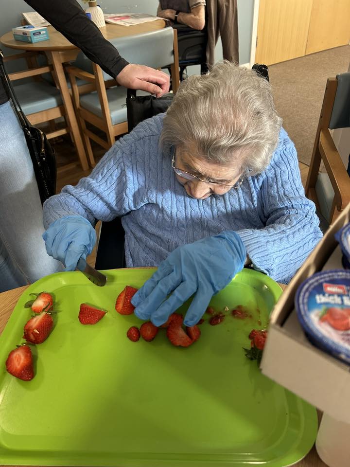 older lady sat down with blue gloves cutting strawberries