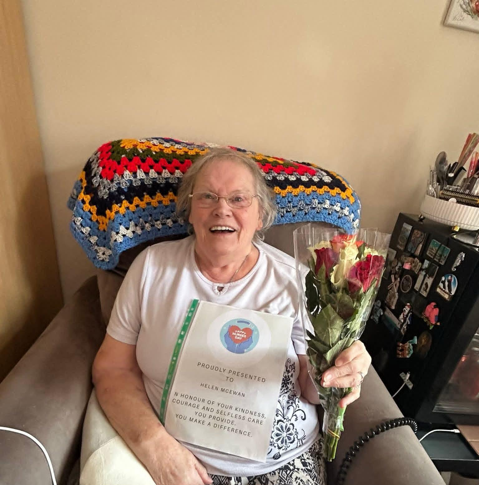 female care home resident holding a bunch of flowers and a certificate, smiling