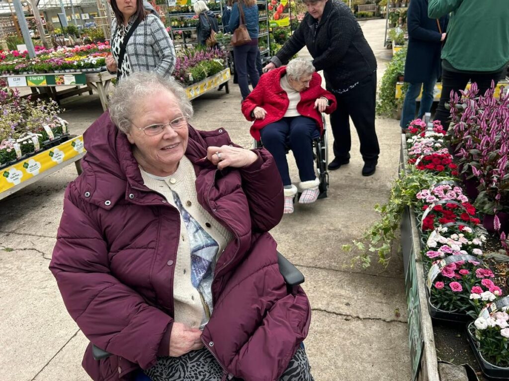 elderly woman in wheelchair smiling in a garden centre